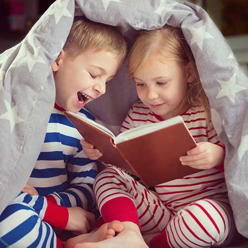 Geschwister zusammen beim Lesen im Bett unter der Decke.