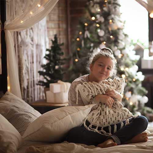 Mädchen mit Kuschelkissen - im Hintergrund ein Weihnachtsbaum.